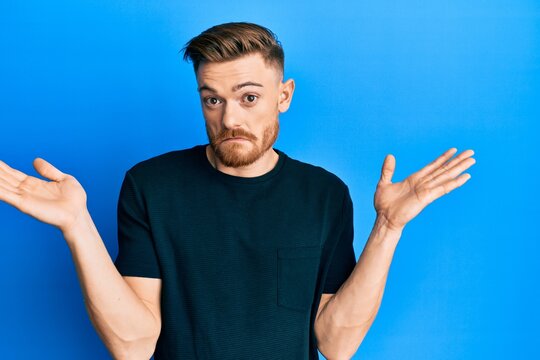 Young redhead man wearing casual black t shirt clueless and confused with open arms, no idea and doubtful face.