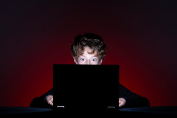 Surprised boy with computer surfing the internet alone on dark background