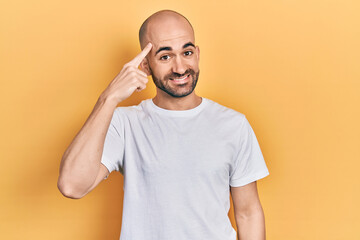 Fototapeta na wymiar Young bald man wearing casual white t shirt smiling pointing to head with one finger, great idea or thought, good memory