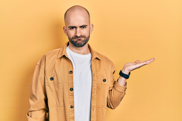 Young bald man presenting with open palms, holding something depressed and worry for distress, crying angry and afraid. sad expression.