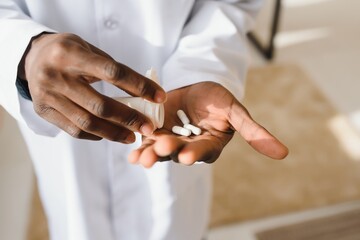 Hand of african american doctor holding pills over white studio background, cropped