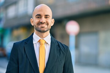 Fototapeta premium Young hispanic bald businessman smiling happy standing at the city.