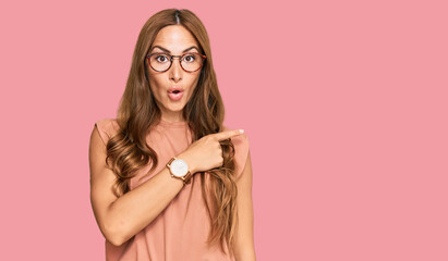 Young hispanic woman wearing casual clothes and glasses surprised pointing with finger to the side, open mouth amazed expression.