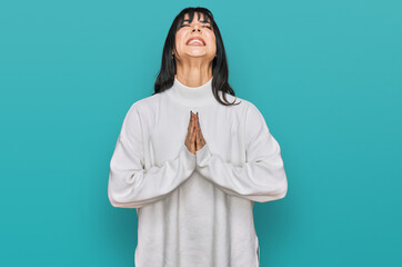 Young brunette woman with bangs wearing casual turtleneck sweater begging and praying with hands...