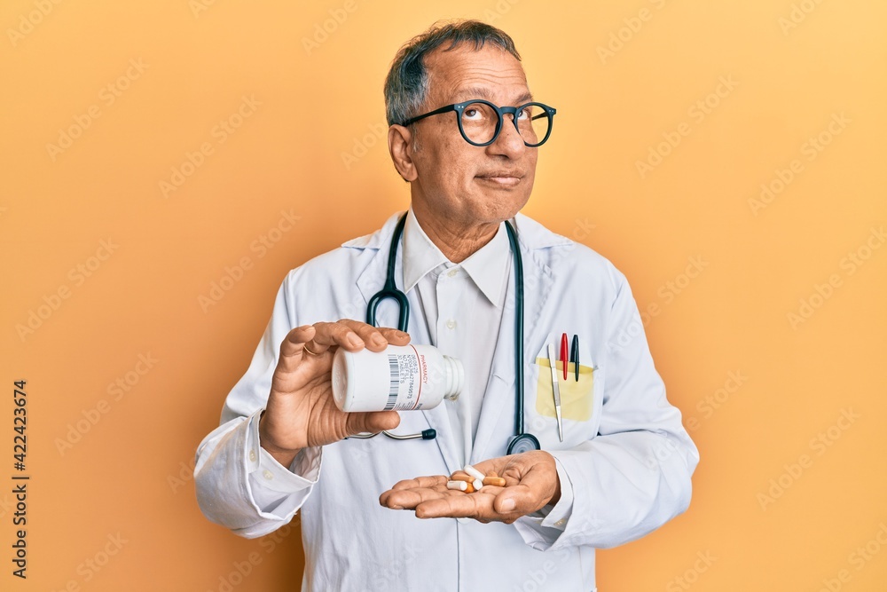 Poster middle age indian man wearing doctor uniform holding prescription pills smiling looking to the side 