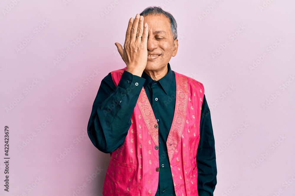 Poster Middle age indian man wearing traditional indian clothes covering one eye with hand, confident smile on face and surprise emotion.