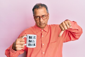 Middle age indian man drinking mug of coffee with best dad ever message with angry face, negative sign showing dislike with thumbs down, rejection concept