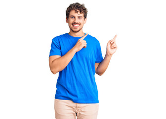 Young handsome man with curly hair wearing casual clothes smiling and looking at the camera pointing with two hands and fingers to the side.