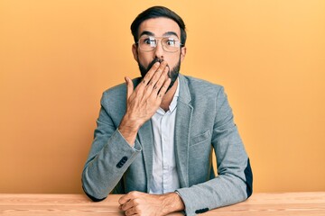 Young hispanic man working at the office covering mouth with hand, shocked and afraid for mistake....