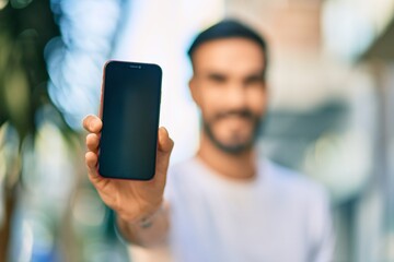 Young hispanic man smiling happy showing screen smartphone at the city.