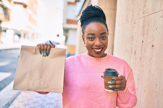 Young african american woman holding delivery paper bag and take away coffee at the city.