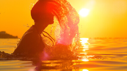 LENS FLARE: Scenic view of a young woman splashing ocean water with her hair.