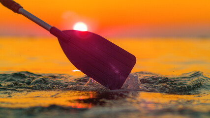 SILHOUETTE: Golden sunset shines on the kayaker's paddle splashing ocean water.