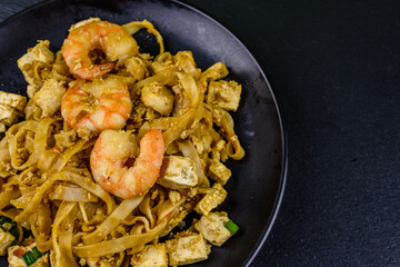 Black plate with pad thai on a slate board. Top view
