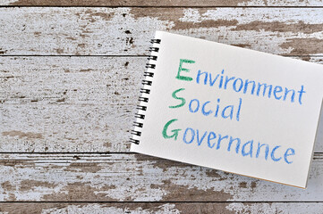 There is a note book with "Environment, Social, Governance" written on it.It was on top of white damaged wood table.