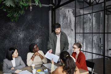 Portrait of contemporary bearded businessman giving presentation to colleagues during meeting in...