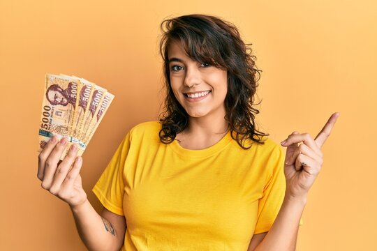 Young hispanic woman holding 5000 hungarian forint banknotes smiling happy pointing with hand and finger to the side