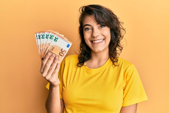 Young hispanic woman holding bunch of 50 euro banknotes looking positive and happy standing and smiling with a confident smile showing teeth