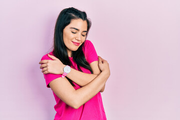 Obraz na płótnie Canvas Young hispanic girl wearing casual pink t shirt hugging oneself happy and positive, smiling confident. self love and self care