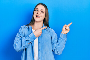 Young hispanic girl wearing casual clothes and glasses smiling and looking at the camera pointing with two hands and fingers to the side.