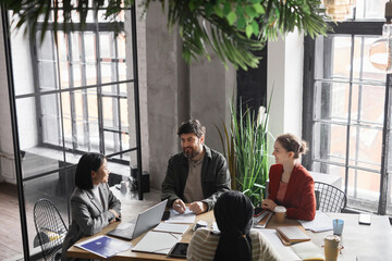 High angle view at diverse business team discussing project at meeting table focus on bearded man smiling at colleagues, copy space