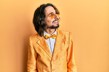 Young hispanic man wearing hipster elegant look looking away to side with smile on face, natural...
