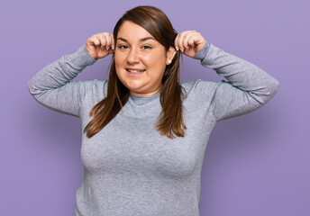 Beautiful brunette plus size woman wearing casual clothes smiling pulling ears with fingers, funny...