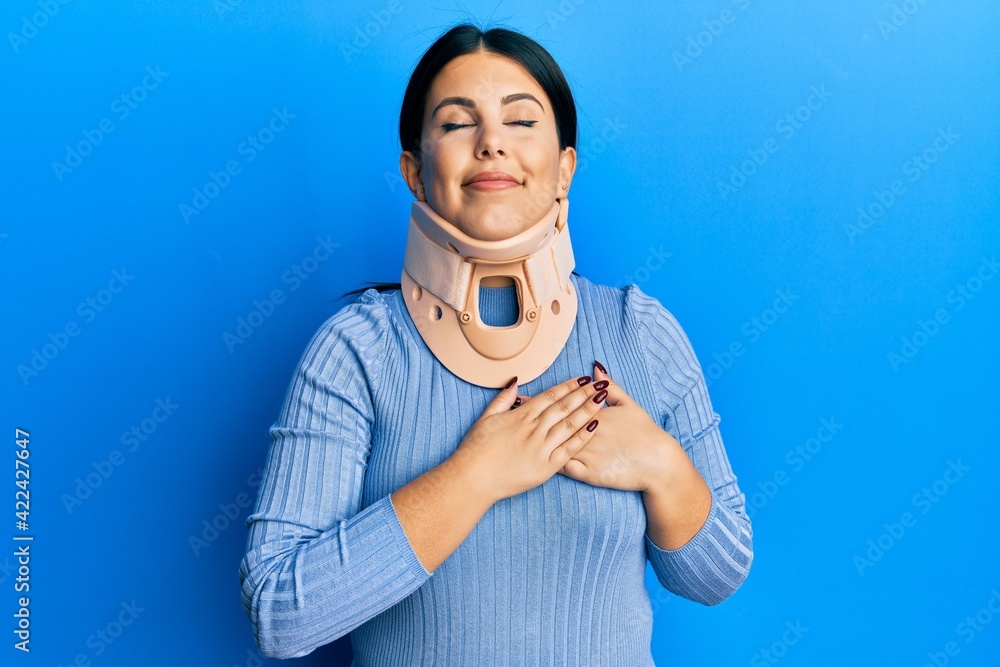 Canvas Prints Beautiful brunette woman wearing cervical collar smiling with hands on chest with closed eyes and grateful gesture on face. health concept.