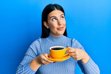 Beautiful brunette woman drinking a yellow cup of black coffee smiling looking to the side and staring away thinking.