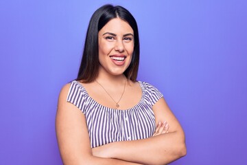 Obraz premium Young beautiful brunette woman wearing casual striped t-shirt standing over purple background happy face smiling with crossed arms looking at the camera. Positive person.