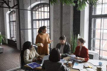 Diverse group of business people collaborating at meeting table in graphic office interior, copy...