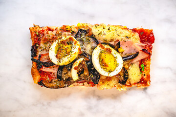 Pizza slice with tomato sauce, fried eggplant, ham, mozzarella cheese and boiled eggs
