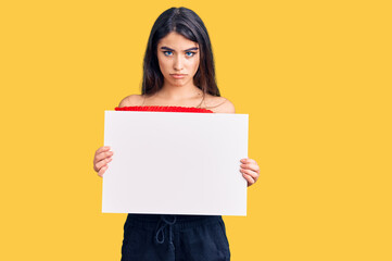 Fototapeta na wymiar Brunette teenager girl holding blank empty banner thinking attitude and sober expression looking self confident
