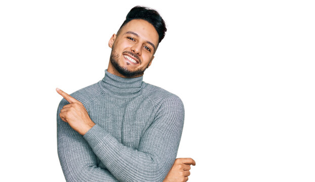 Young arab man wearing casual clothes with a big smile on face, pointing with hand and finger to the side looking at the camera.