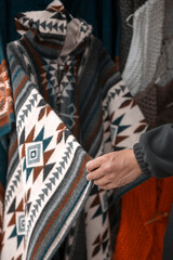 a hand holding and teaching a beautiful knitted poncho with the design of colorful geometric figures, traditional clothing