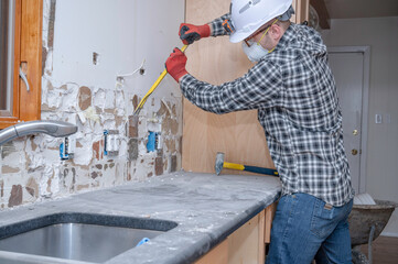 Renovation worker removing tile from kitchen wall