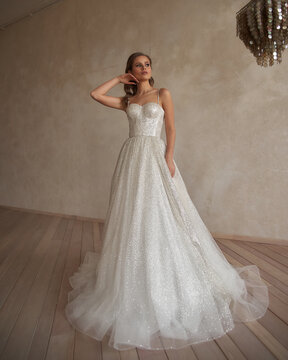 Full length portrait of young beautiful woman wearing white wedding dress. Elegant bride standing and posing against beige wall