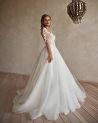 Fototapeta premium Full length portrait of young beautiful woman wearing white wedding dress. Elegant bride standing and posing against beige wall