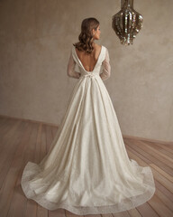 Full length portrait of young beautiful woman wearing white wedding dress. Elegant bride standing and posing against beige wall