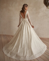 Full length portrait of young beautiful woman wearing white wedding dress. Elegant bride standing and posing against beige wall