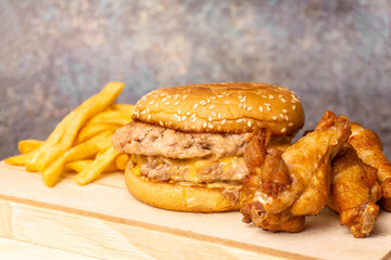 Double burger with cheddar cheese no vegetable, French-fries, and fried chicken on a wooden plate.