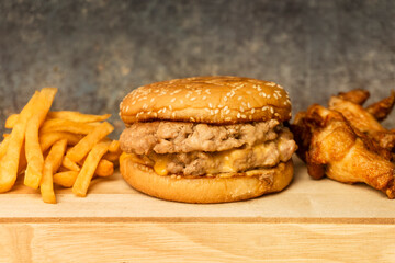 Double burger with cheddar cheese no vegetable, French-fries, and fried chicken on a wooden plate.