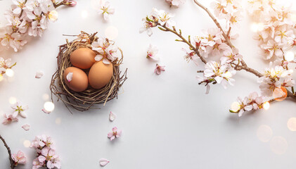 Easter eggs in nest and pink flowering sakura branches on white background with bokeh, light. Happy Easter holiday, top view, flat lay