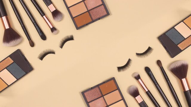 Blinking eye lashes with make up brushes and eye shadow palettes on beige background. Stop motion