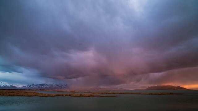 Time lapse of rain storm lighting up during colorful sunset moving over Utah Lake.