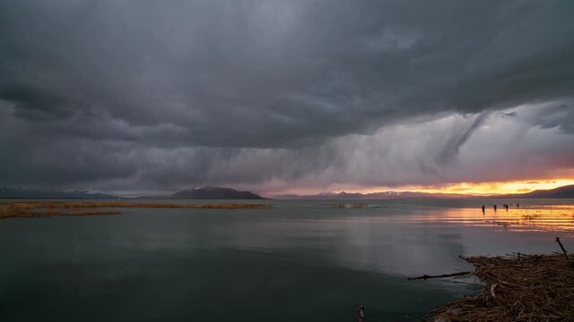 Time lapse of rain storm moving over Utah Lake with fishermen standing in the water during sunset into dusk.