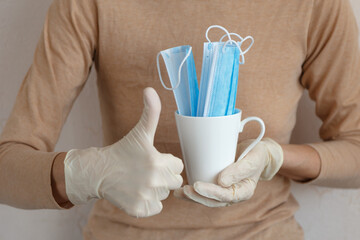 Hand in white gloves holding a ceramic cup with blue masks and other hand showing thumb up