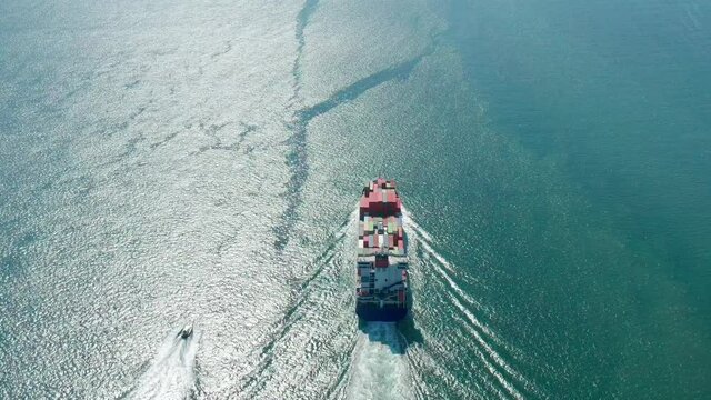 A cargo ship transports containers towards open ocean waters. Aerial view of a small and a huge merchant vessels sailing across the Atlantic Ocean. High quality 4k footage