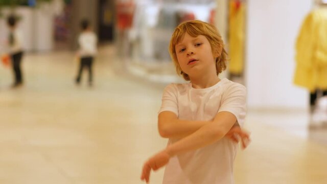 Blonde boy shows different emotions at camera in shopping mall.