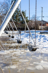 Spring in the park with swings at the playground and melting snow on the ground. Springtime in Ottawa, Canada